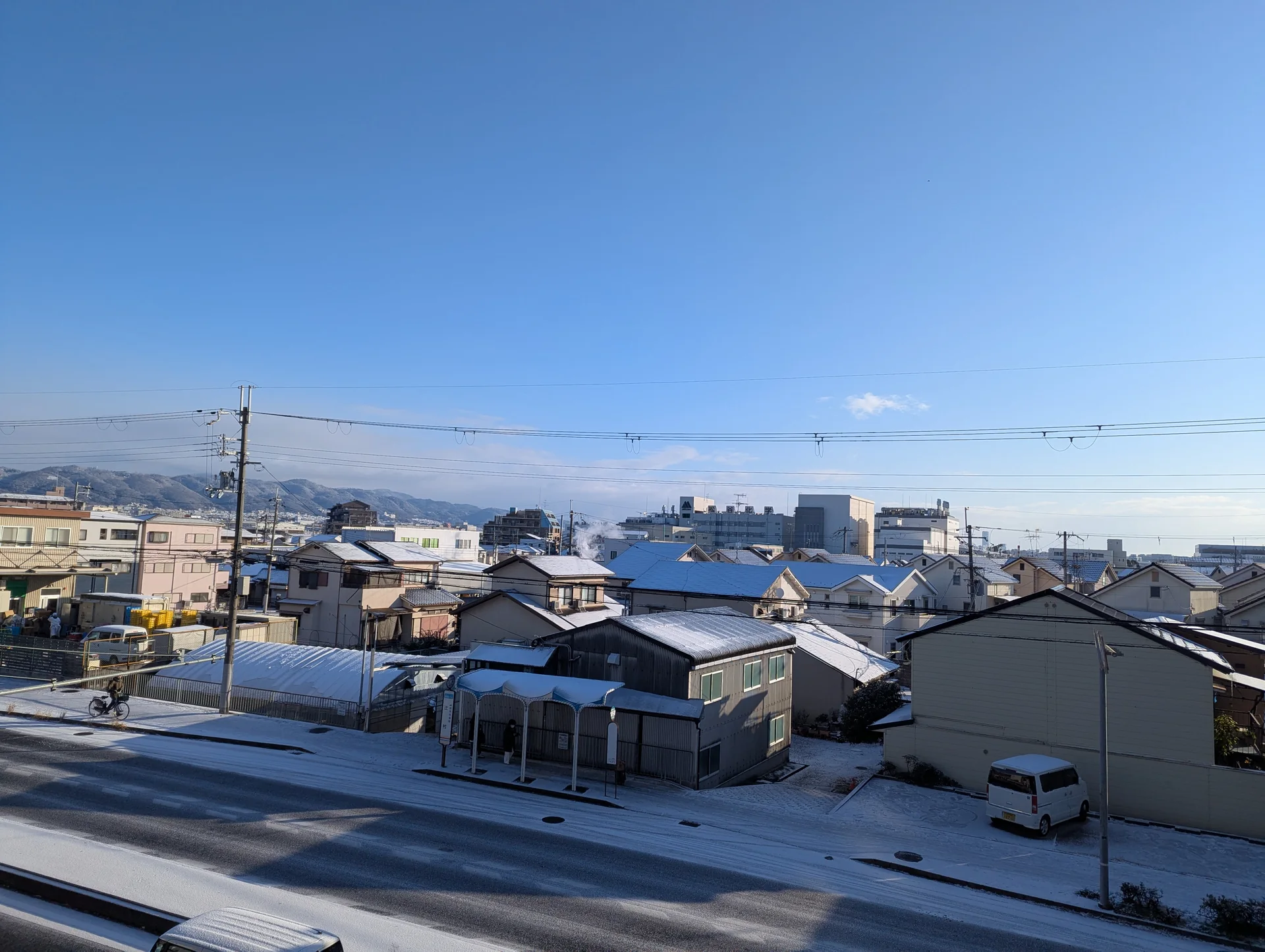 緑道から見渡す、雪をかぶった家々の屋根と道路、青い冬の空